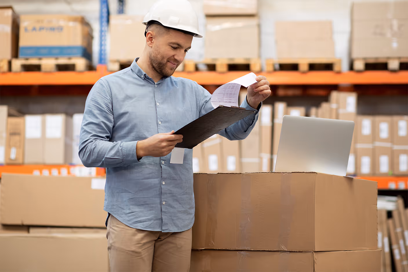 Warehouse operator reviewing inventory paperwork beside a laptop